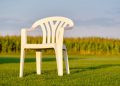 Empy white plastic garden chair standing on a green lawn in front of a cornfield in evening light. Seen in Bavaria, Germany in August.